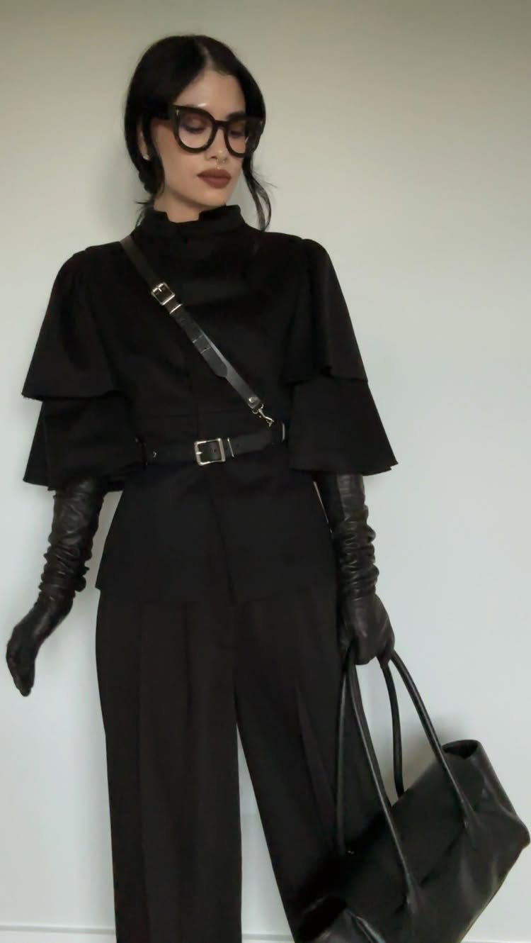 Woman in an all-black winter outfit featuring long leather gloves, a belt, and a large tote bag.