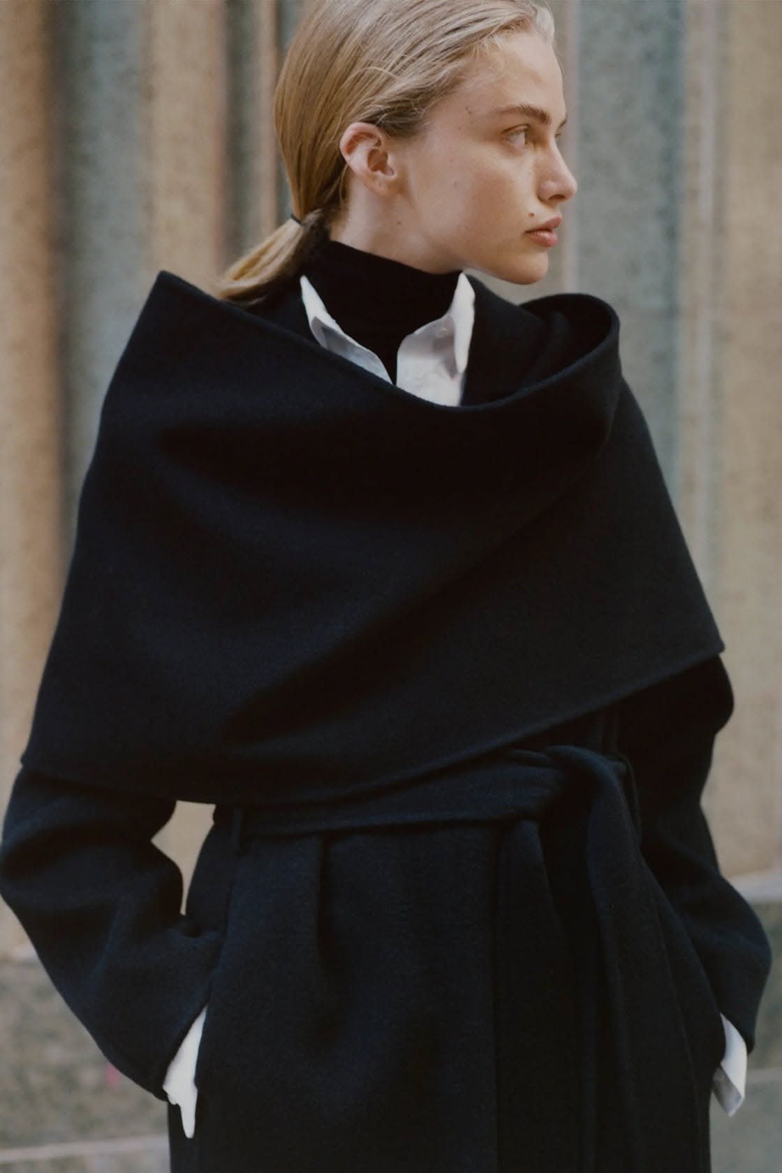 A woman wearing a dramatic black wrap coat with a large shawl collar and a white shirt underneath.