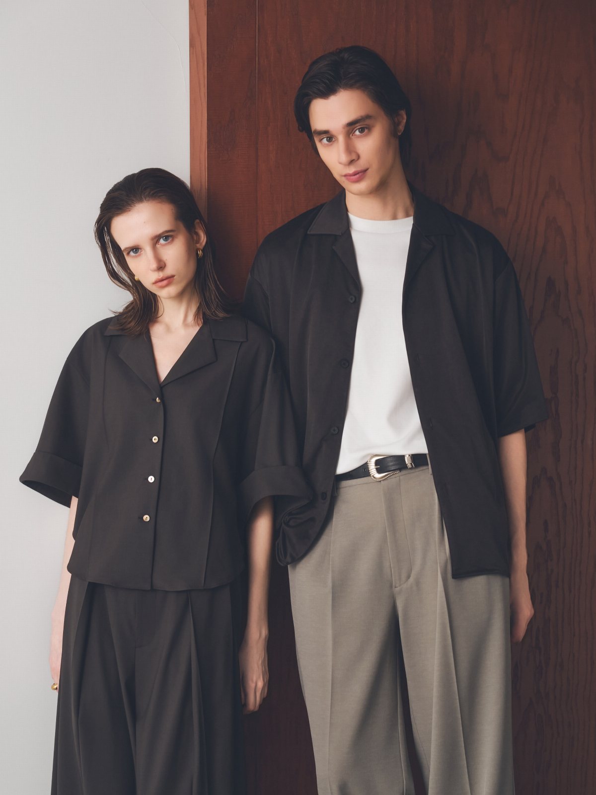 Two models posing in dark and light colored casual work trousers and shirts.