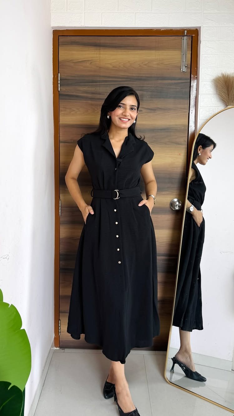 A woman wearing a black button-down midi dress and black heels standing near a mirror.