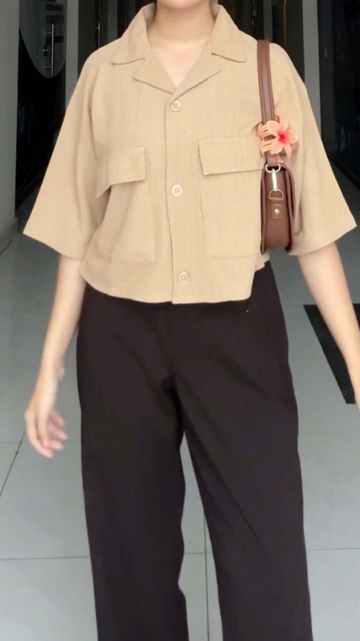 Person wearing a beige short-sleeved utility shirt and dark brown wide-leg trousers.