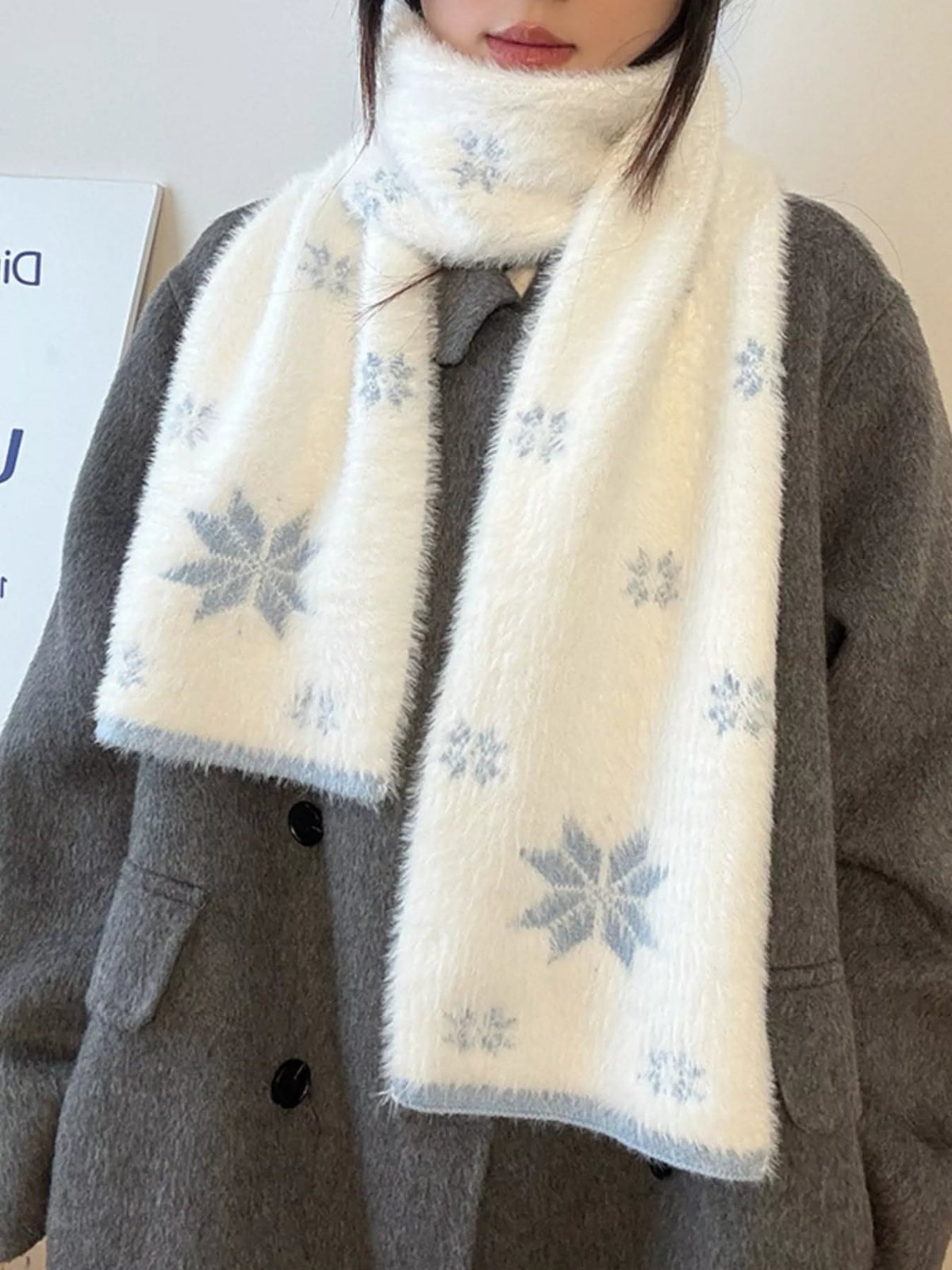 A person wearing a grey coat and a white fuzzy scarf with blue snowflake patterns.