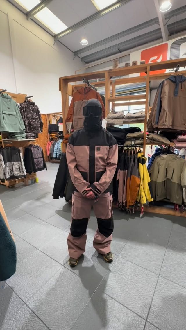 A mannequin wearing a pink and black snow suit with goggles in a retail store.