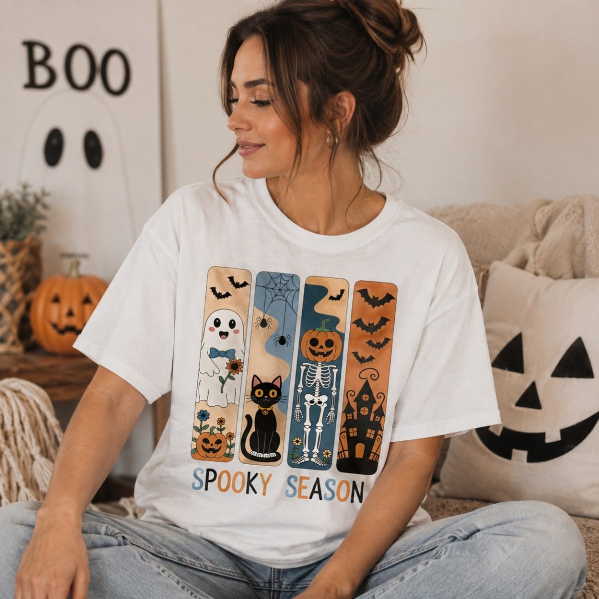 Woman wearing a white graphic t-shirt with colorful Halloween illustrations and spooky season text.