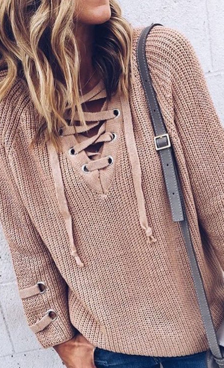 A person wearing a dusty rose chunky knit sweater with a lace-up neckline and drawstring details.