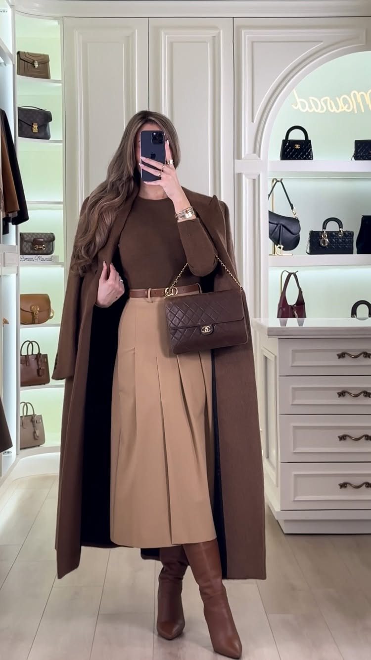 Woman wearing a brown long-sleeve top, tan midi skirt, long brown coat, and brown leather boots.