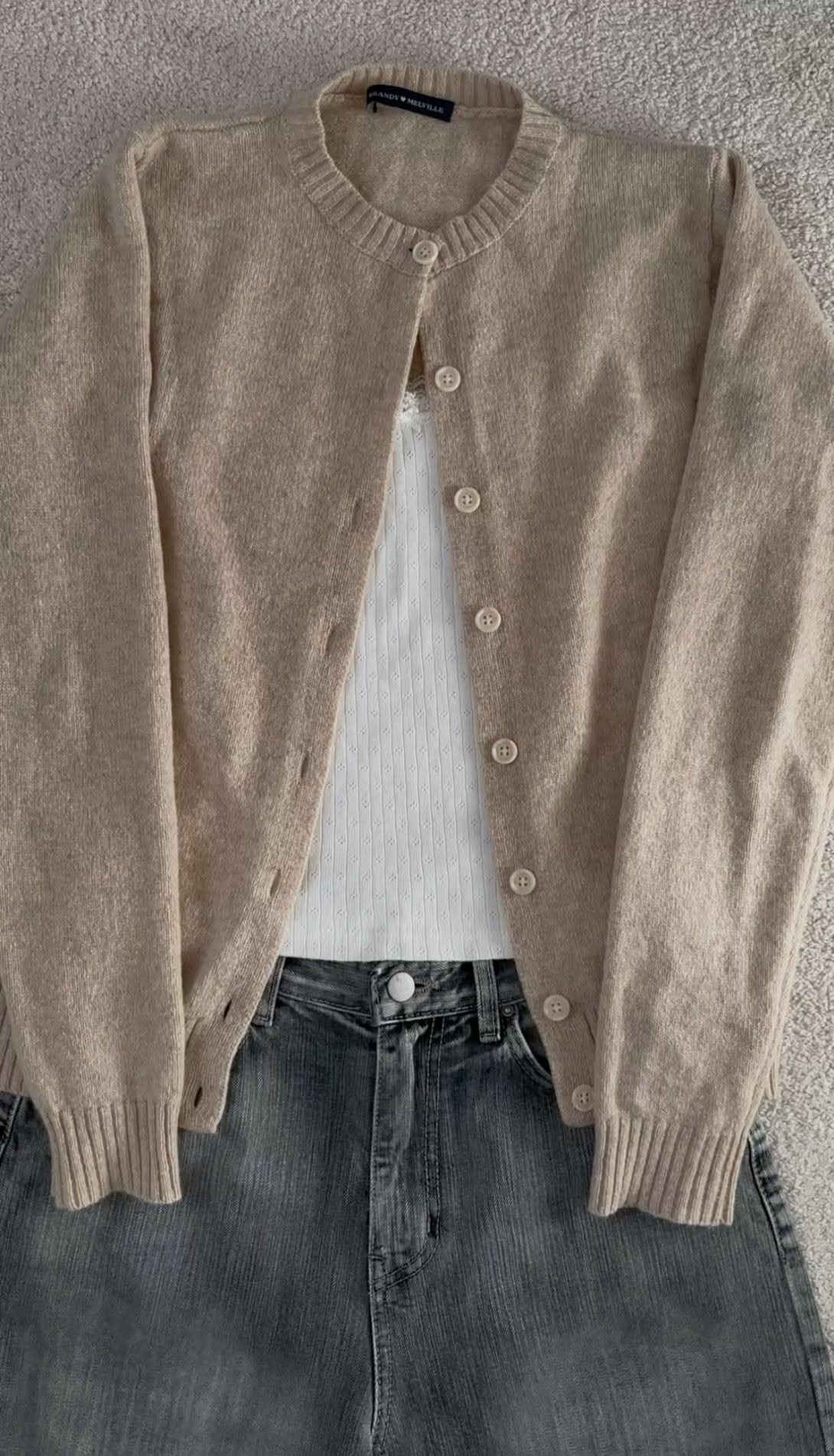 A beige knit cardigan layered over a white shirt and grey denim skirt.