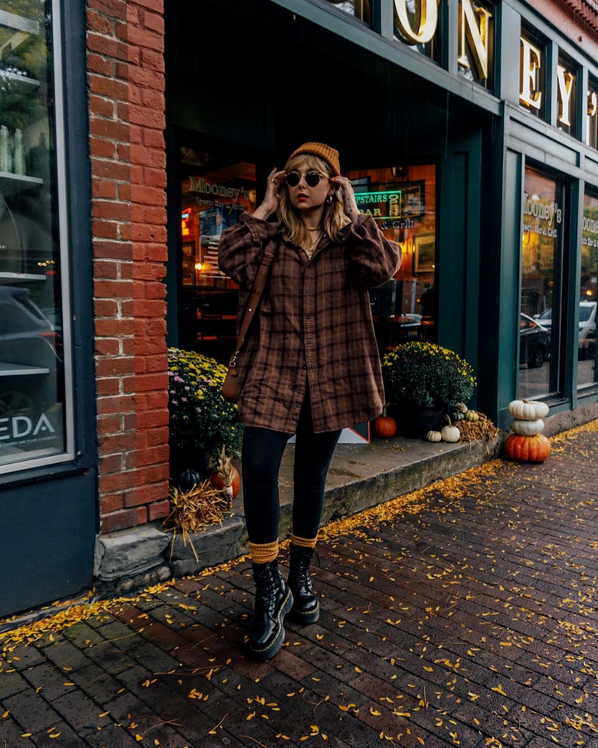 Woman wearing a brown plaid flannel shirt, black leggings, and combat boots on a sidewalk.