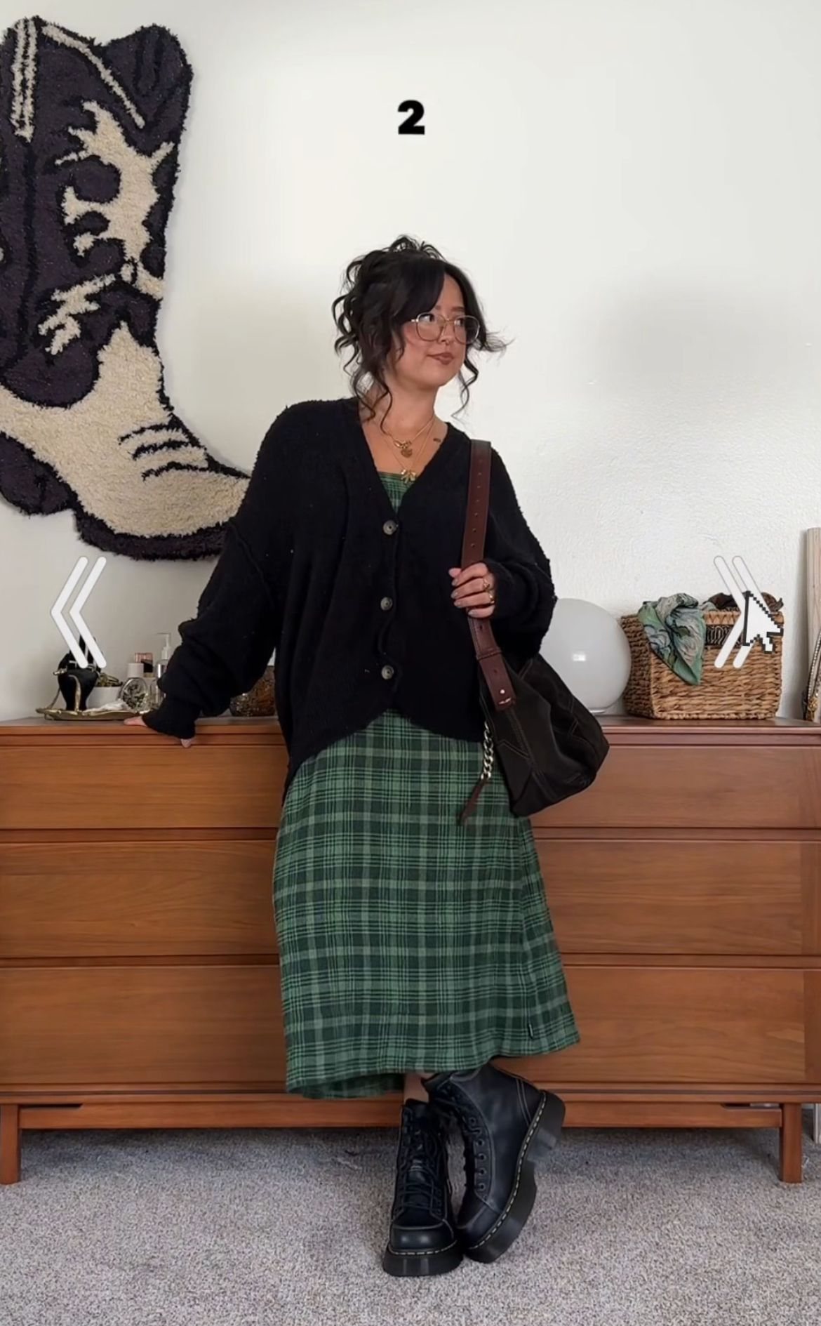 Woman wearing a black cardigan, green plaid skirt, and black boots standing by a dresser.