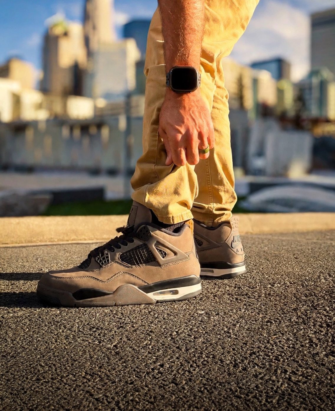 Brown high-top sneakers worn with tan trousers against a blurred city skyline background.
