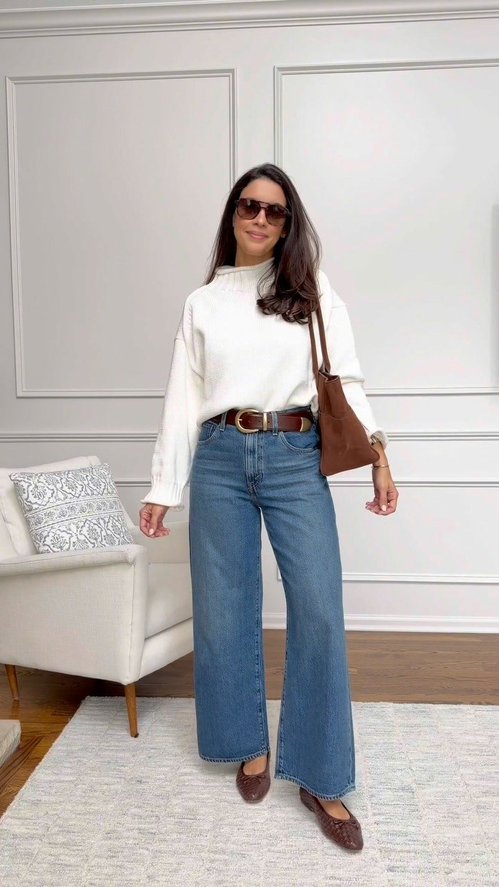 Woman posing in a white sweater, wide-leg blue jeans, and brown ballet flats.