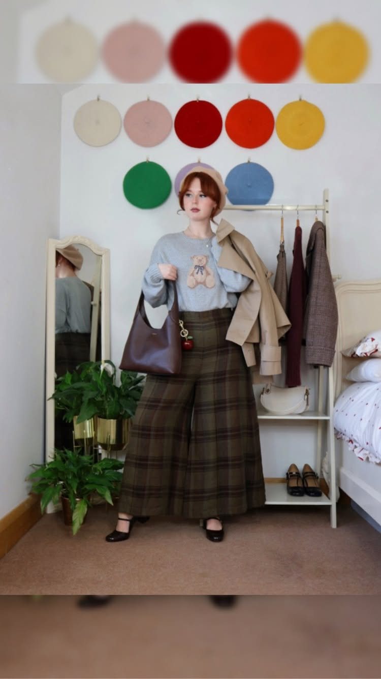 A person wearing a light blue sweater and wide-leg plaid trousers with black flats.