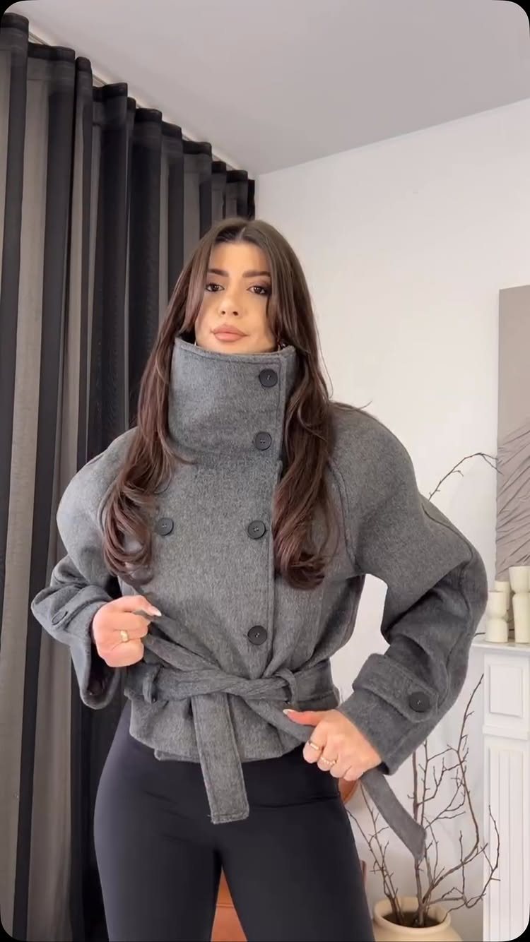 Woman wearing a grey belted wool coat and black leggings indoors.