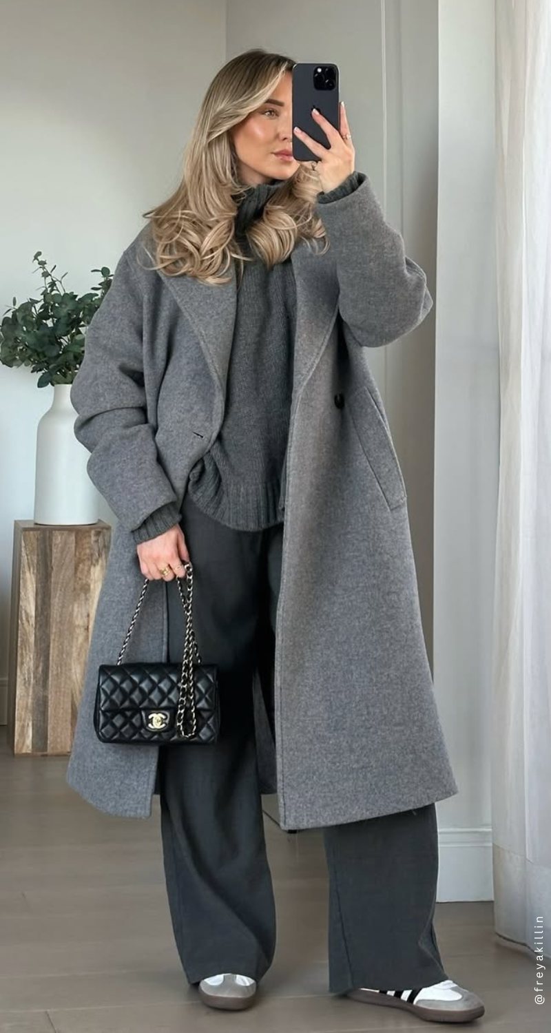 Woman in a grey coat and oversized sweater posing for a mirror selfie.