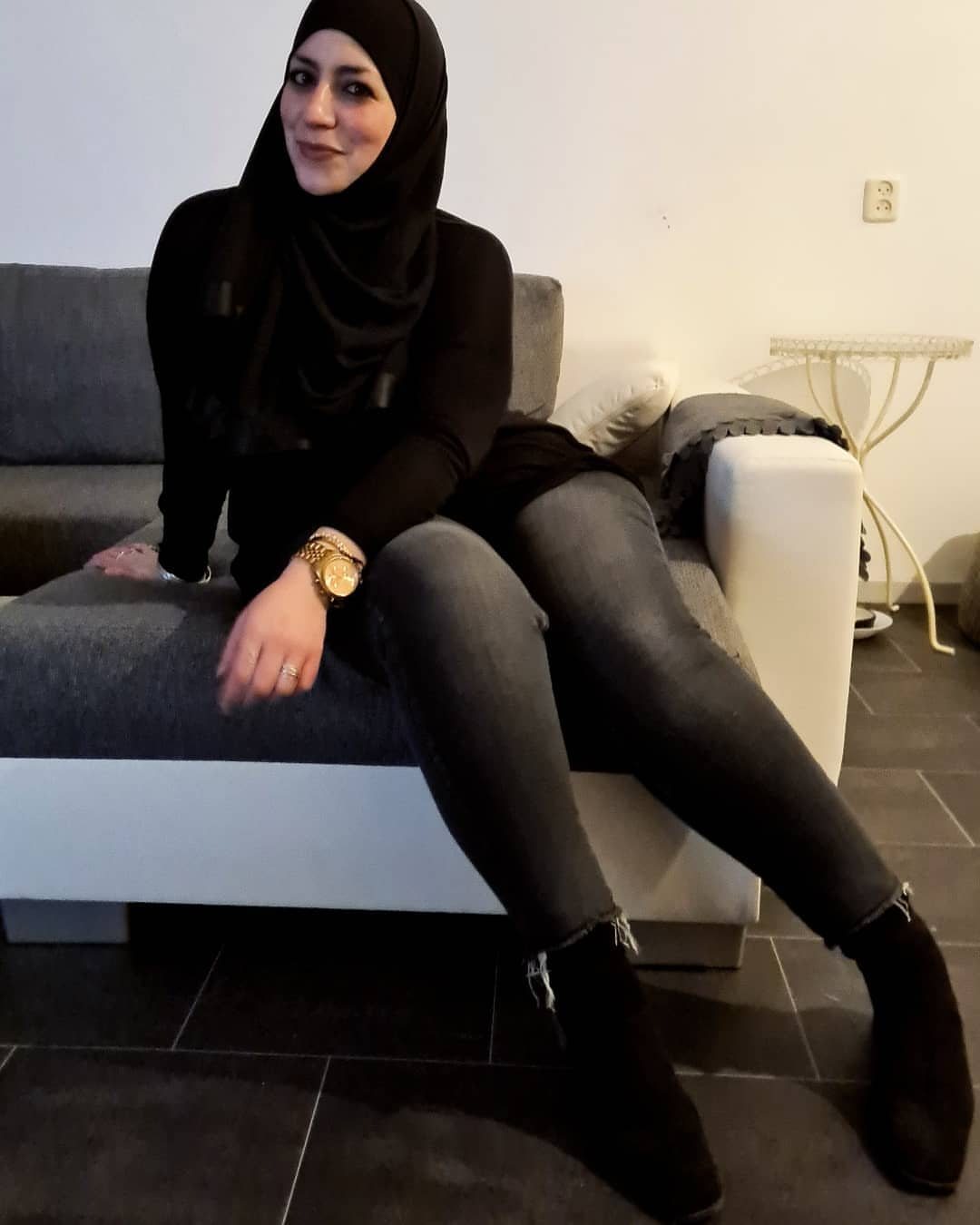 Woman in black hijab and long sleeves wearing grey jeans and black ankle boots.