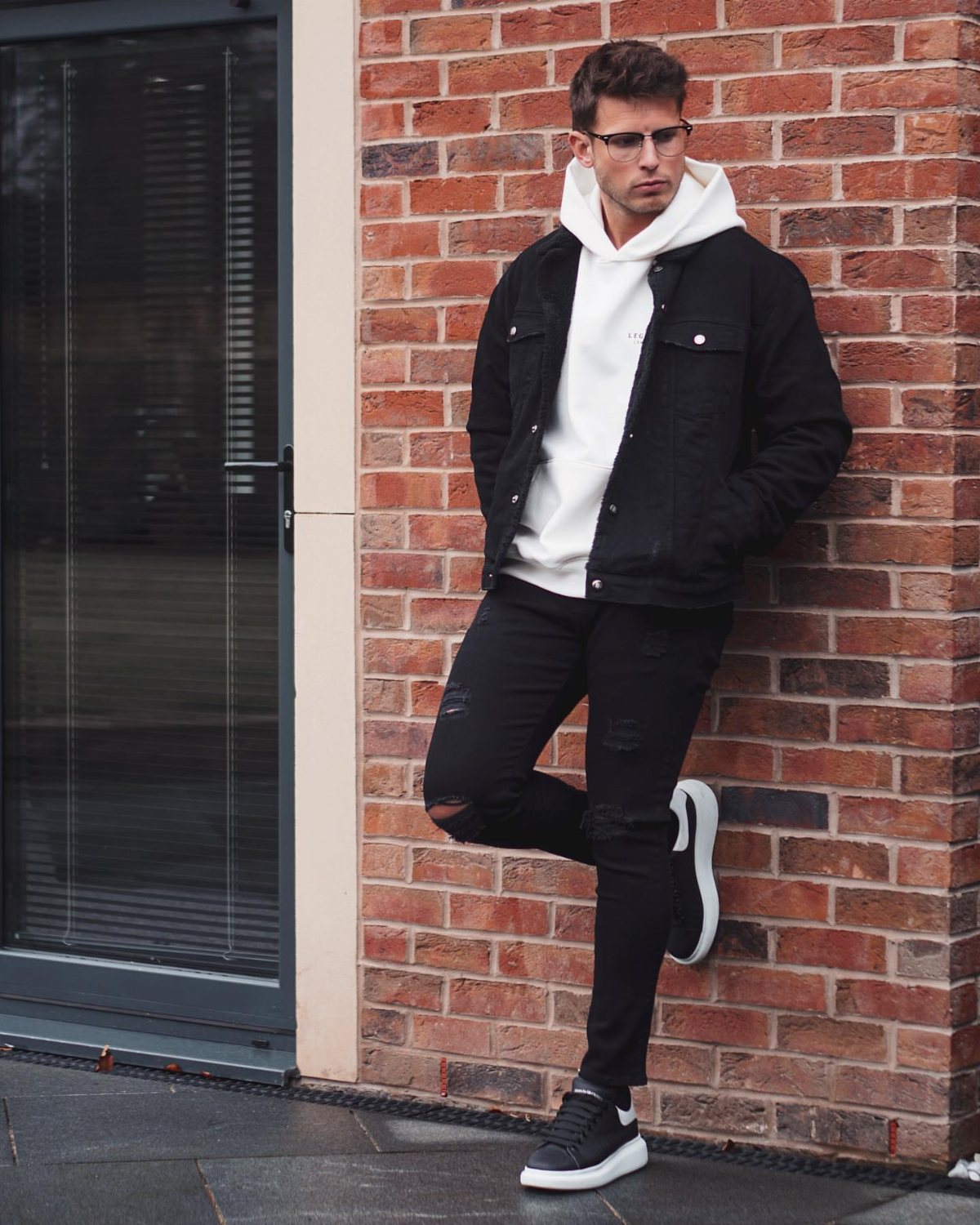 Man in a black denim jacket layered over a white hoodie and black jeans.