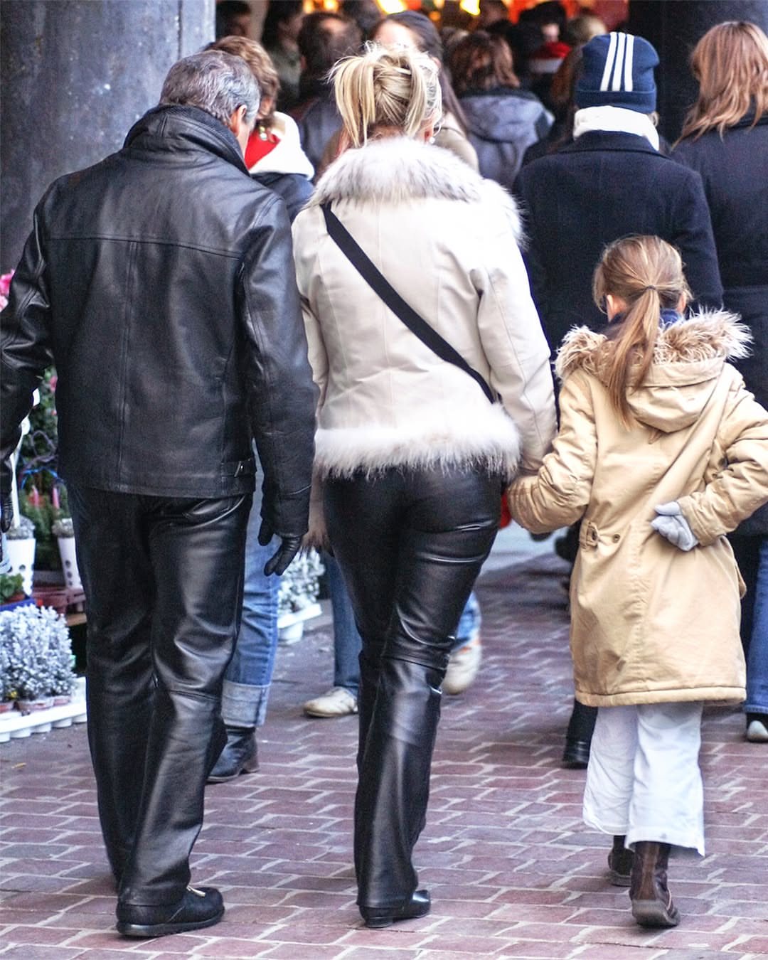 A woman walking in a white fur jacket and black leather pants on a brick street.