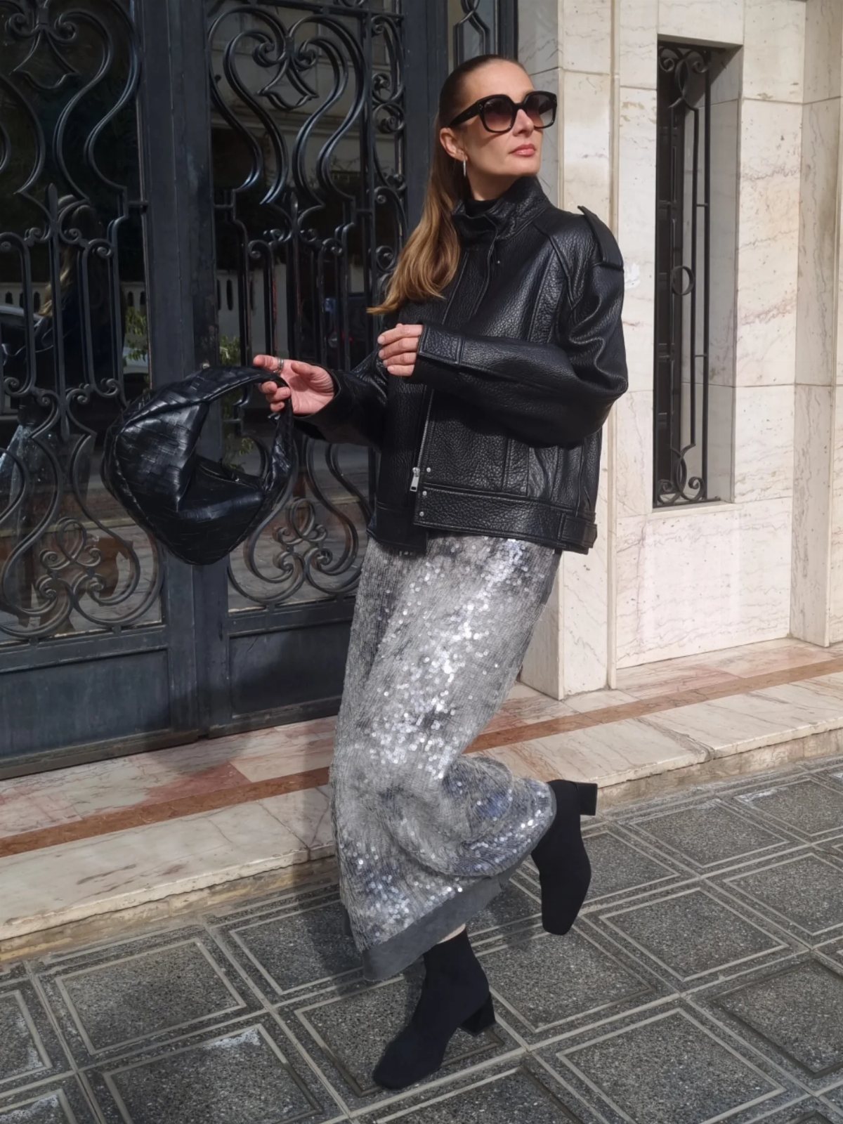 Woman walking in a black leather jacket and a shimmering silver sequined skirt.