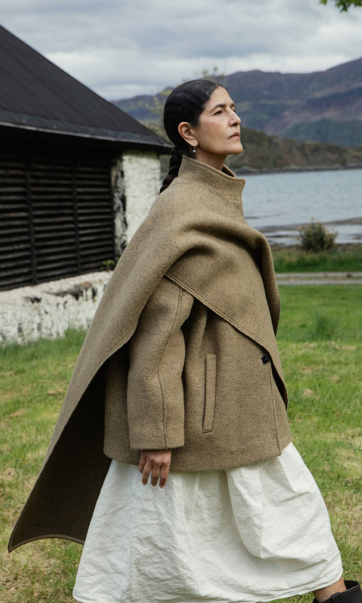 Woman wearing a taupe heavy wool coat with a high funnel neck in a grassy field.