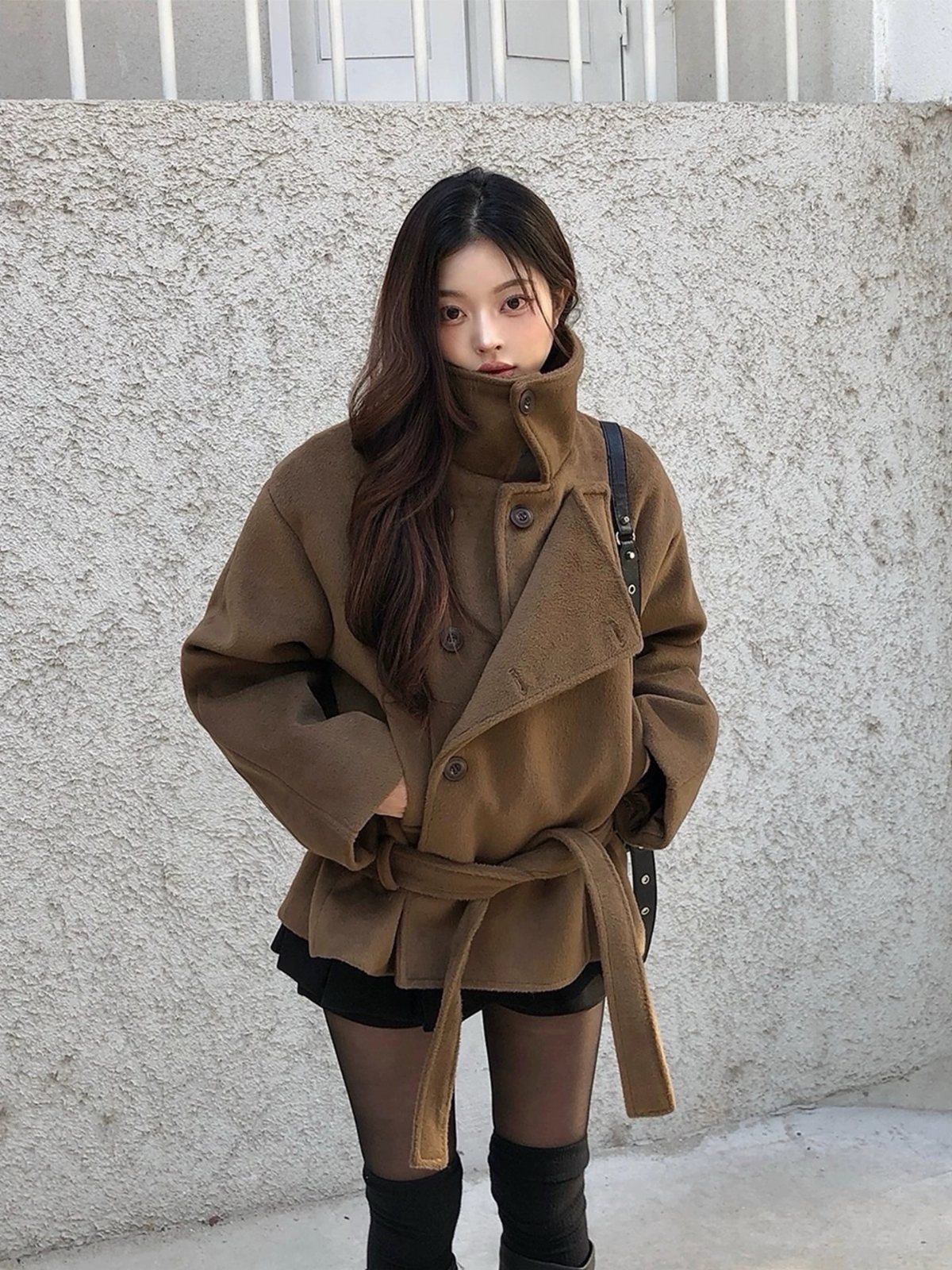 Woman wearing an oversized brown coat cinched with a matching belt over black clothing.