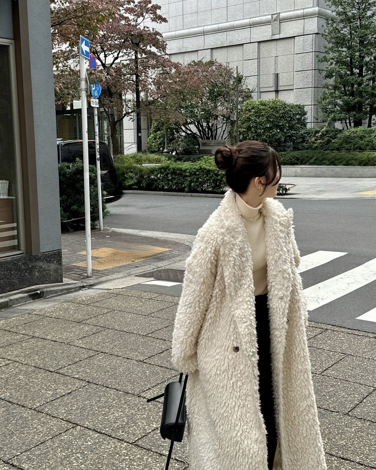 A woman wearing a cream teddy coat and a beige turtleneck sweater standing on a city street.