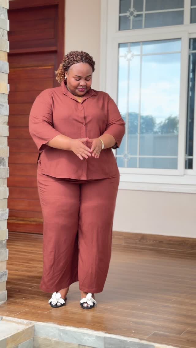 A woman posing in a terracotta two-piece shirt and wide-leg pants set.