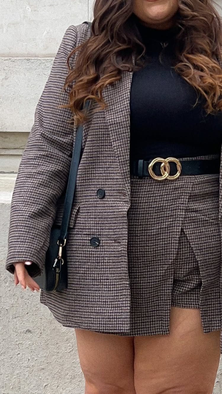 Person wearing a black turtleneck, patterned blazer, and matching skirt with a gold buckle belt.