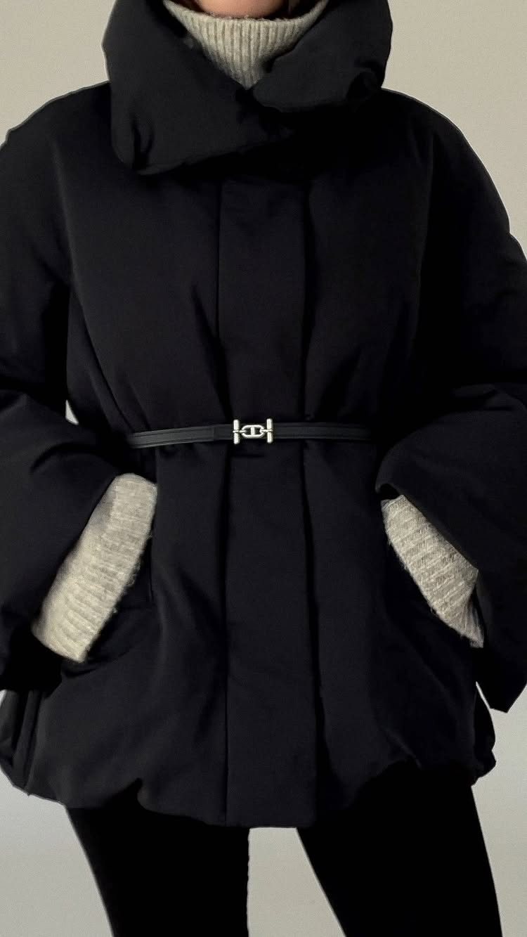 Person wearing a black belted puffer jacket with a grey turtleneck and black leggings.