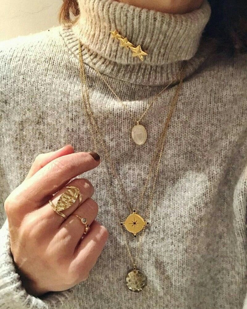 Gold necklaces and rings worn over a grey knit turtleneck sweater.