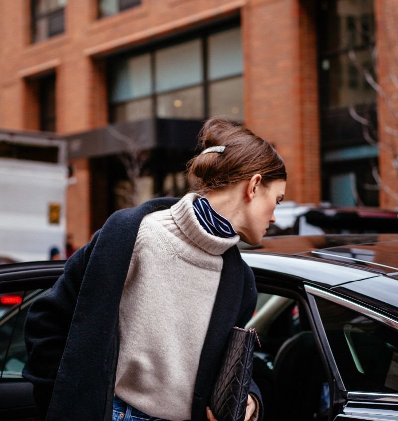 Woman wearing a beige turtleneck layered over a striped turtleneck and a dark navy coat.