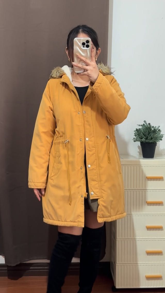 A person posing in a long mustard-yellow parka with a fur-trimmed hood.