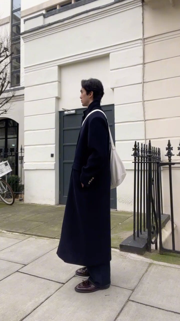 A person wearing a long navy blue relaxed coat and carrying a white tote bag.