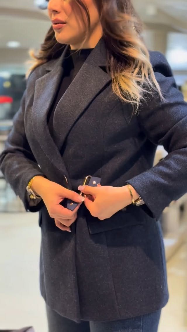 Woman wearing a dark charcoal grey blazer coat over a black turtleneck sweater.