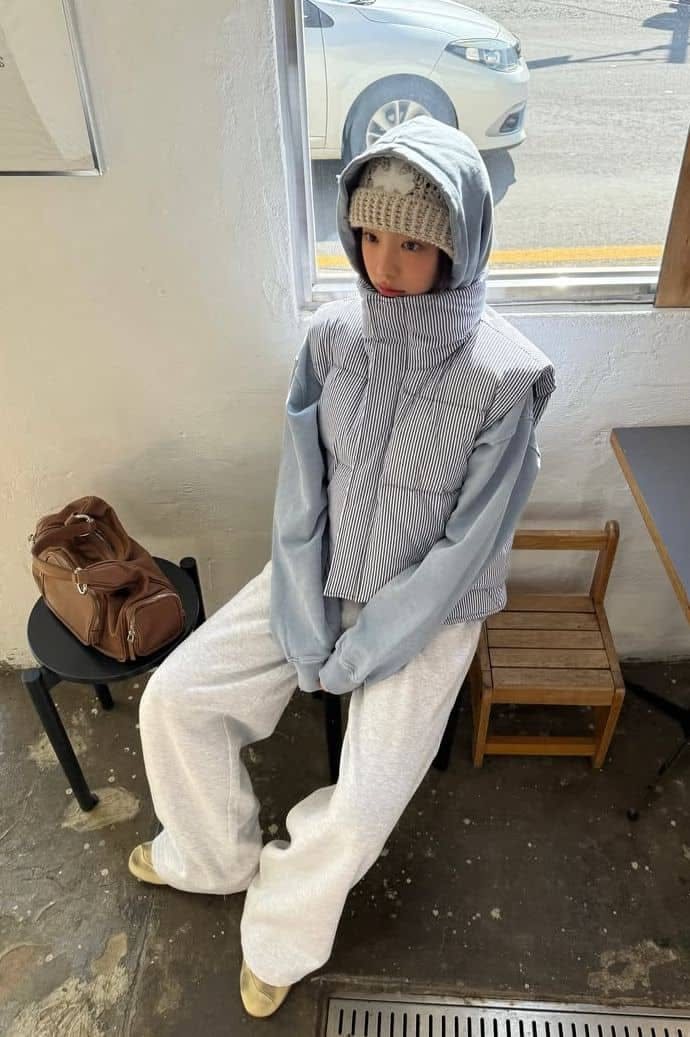 Person wearing a light blue hoodie under a grey quilted vest with white wide-leg pants.