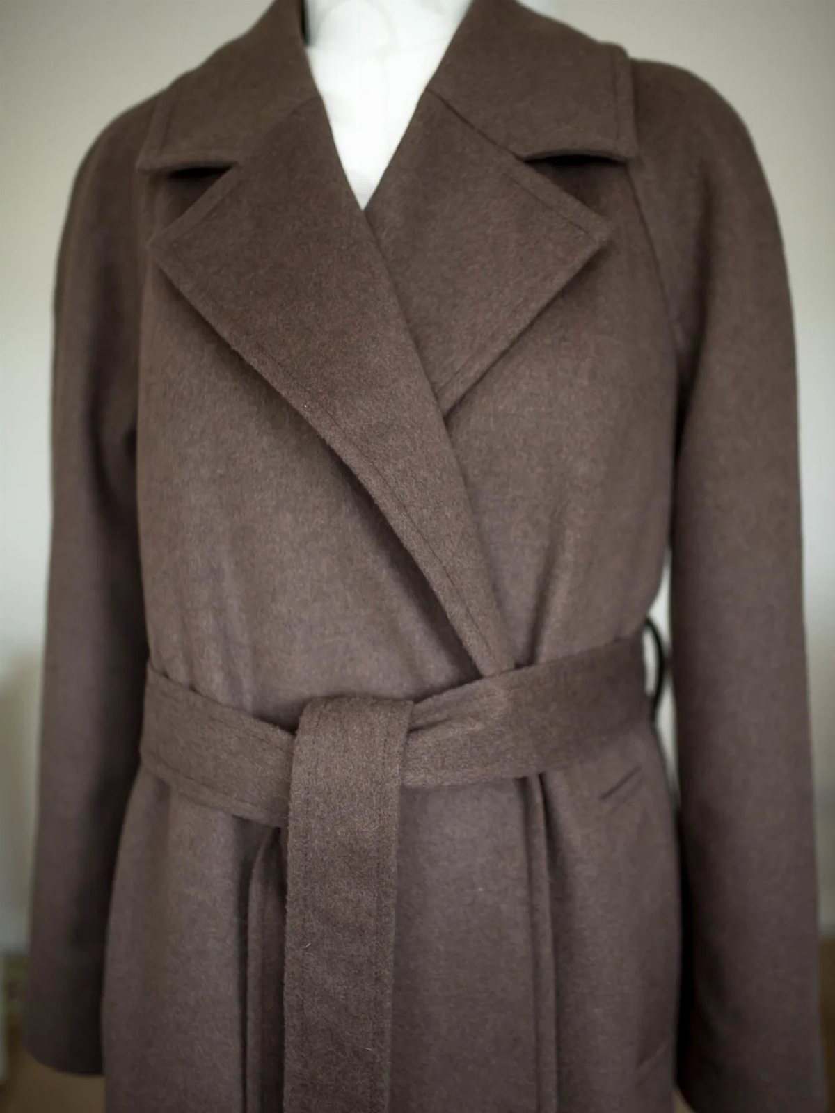 Brown belted wool coat with wide lapels displayed on a white mannequin.