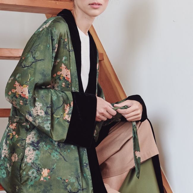 A person wearing a green floral kimono wrap coat with black velvet trim and a tie.