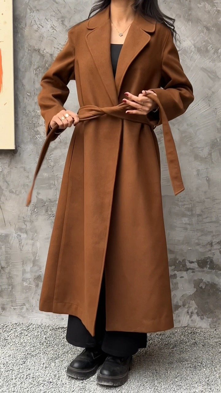 A person wearing a long belted brown wool coat with black trousers and shoes.