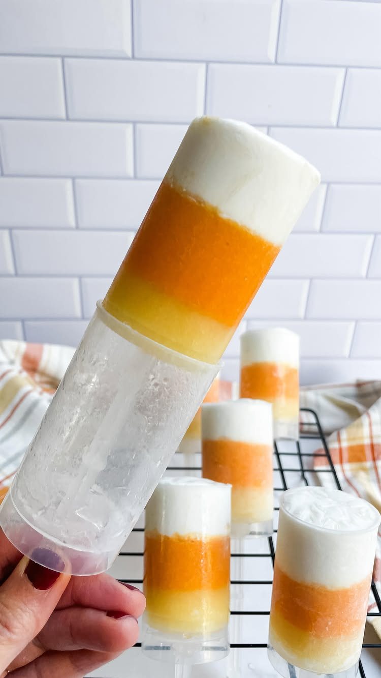 Candy Corn Jello Shots: 4 Layered Recipes for Halloween 3 Layered white, orange, and yellow jello shots in clear plastic tubes on a cooling rack.