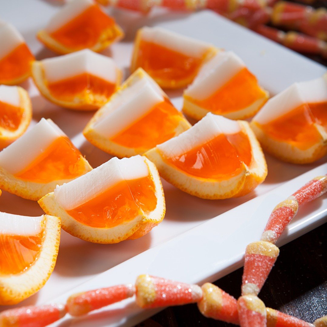 Candy Corn Jello Shots: 4 Layered Recipes for Halloween 4 Triangular orange and white jello shots arranged on a white platter with candy corn decorations.