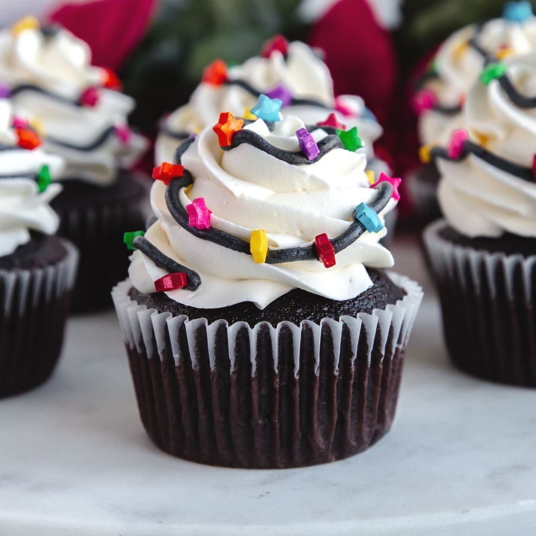 9 Christmas Cupcakes with Santa Hats, Snowmen and Reindeer 7 Chocolate cupcakes with white frosting and colorful candy lights on a white marble surface.
