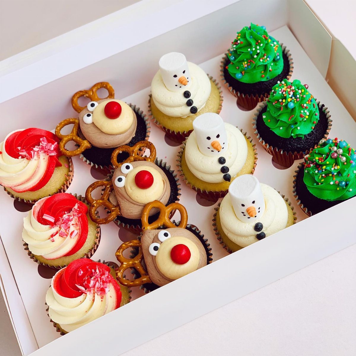 9 Christmas Cupcakes with Santa Hats, Snowmen and Reindeer 6 Assorted Christmas themed cupcakes including reindeer and snowmen in a white cardboard box.