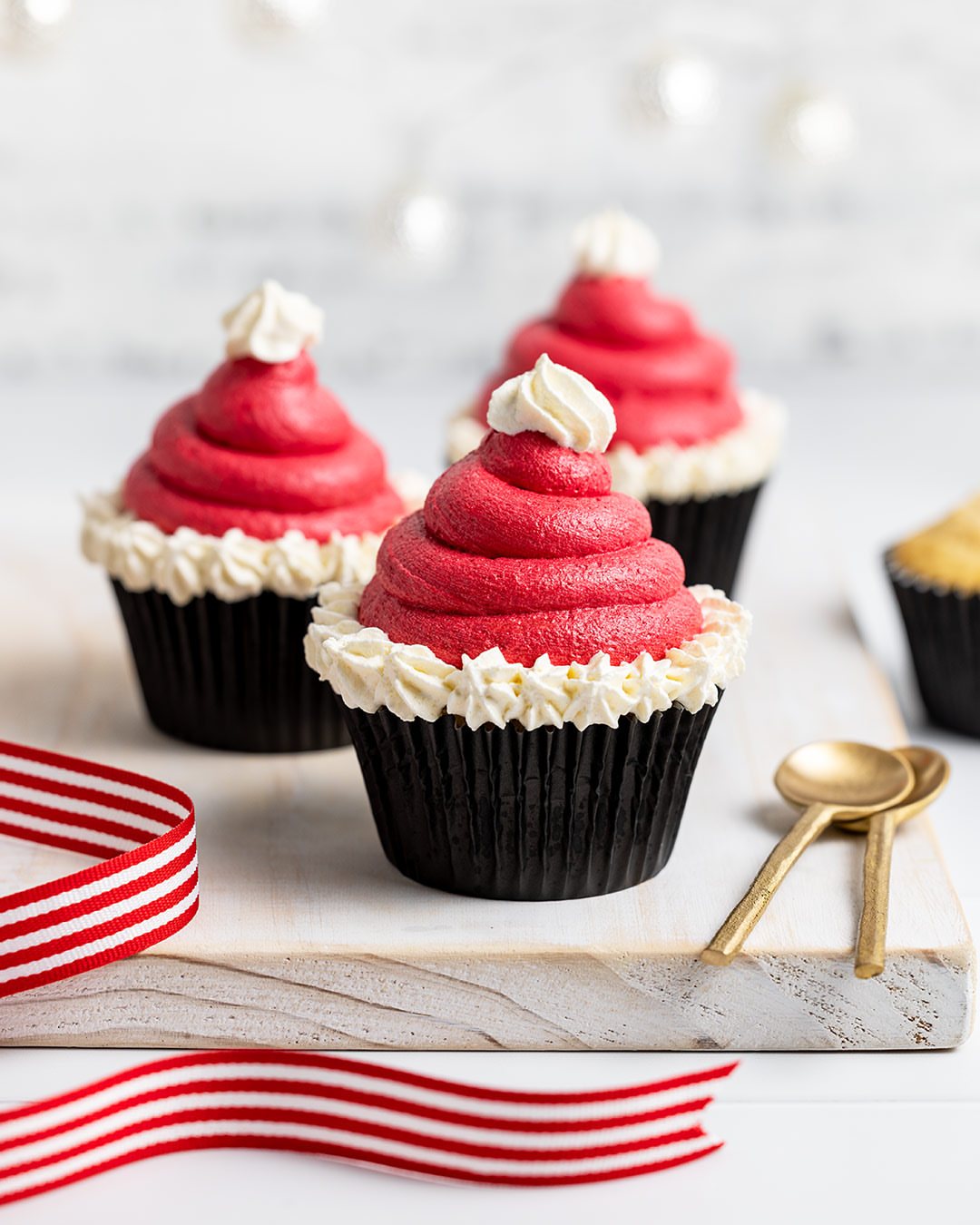 9 Christmas Cupcakes with Santa Hats, Snowmen and Reindeer 5 Three red and white frosting cupcakes shaped like Santa hats on a wooden board.