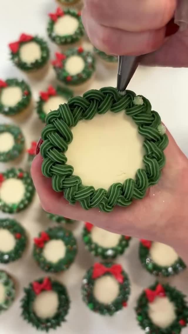 9 Christmas Cupcakes with Santa Hats, Snowmen and Reindeer 2 Hands using a piping bag to create a green frosting wreath on a cupcake.