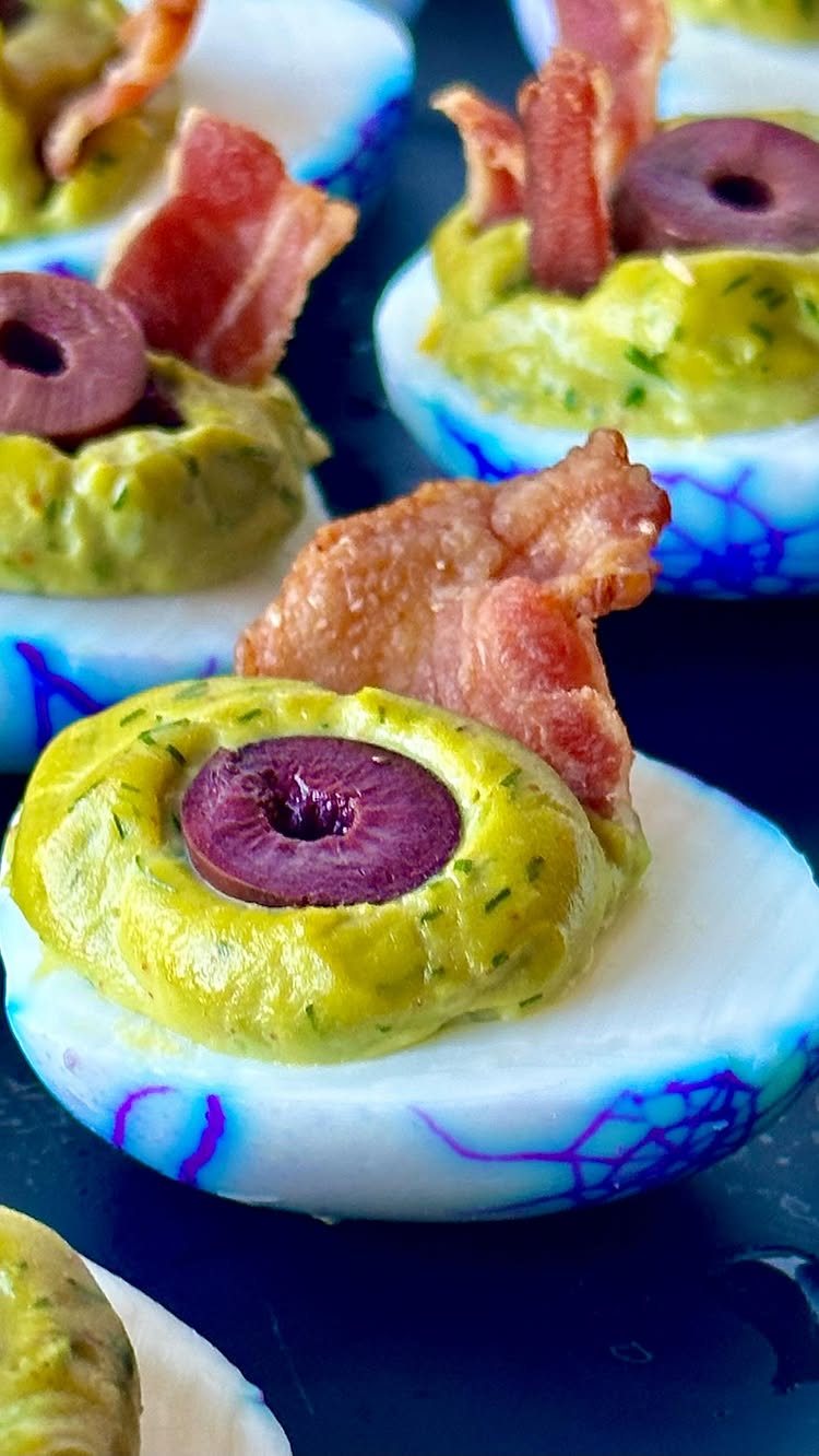 Dyed Deviled Eggs: 5 Ways From Pastel to Bright Pink 4 Blue dyed deviled eggs topped with green filling, a black olive, and crispy bacon bits.