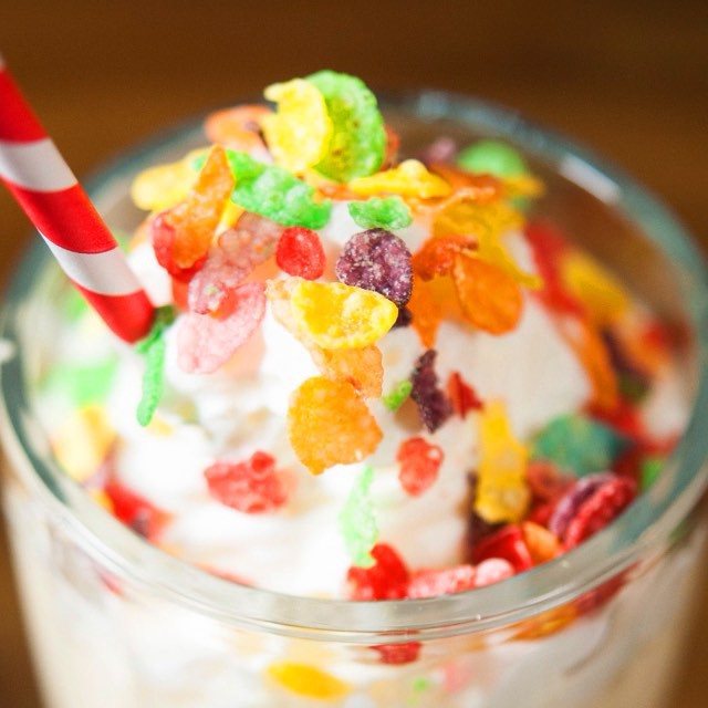 A creamy milkshake topped with whipped cream and colorful Fruity Pebbles cereal in a glass jar.