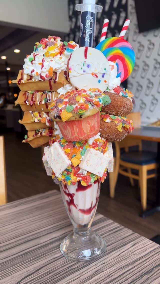 A massive milkshake topped with colorful cereal, donuts, waffles, a lollipop, and whipped cream.