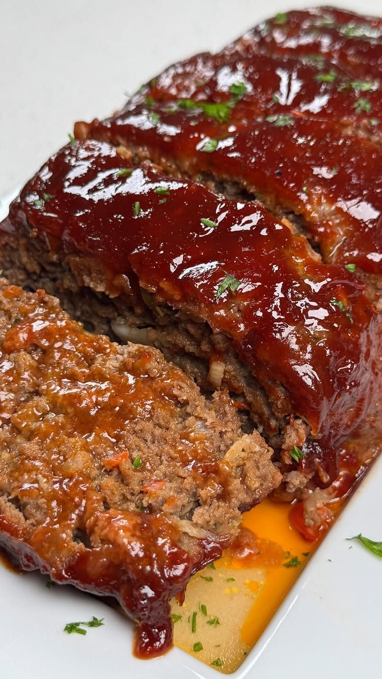 14 Ground Beef Recipes Using Few Ingredients for Low-Stress Weeknights 12 Sliced meatloaf with a glossy red glaze and green herb garnish on a white plate.