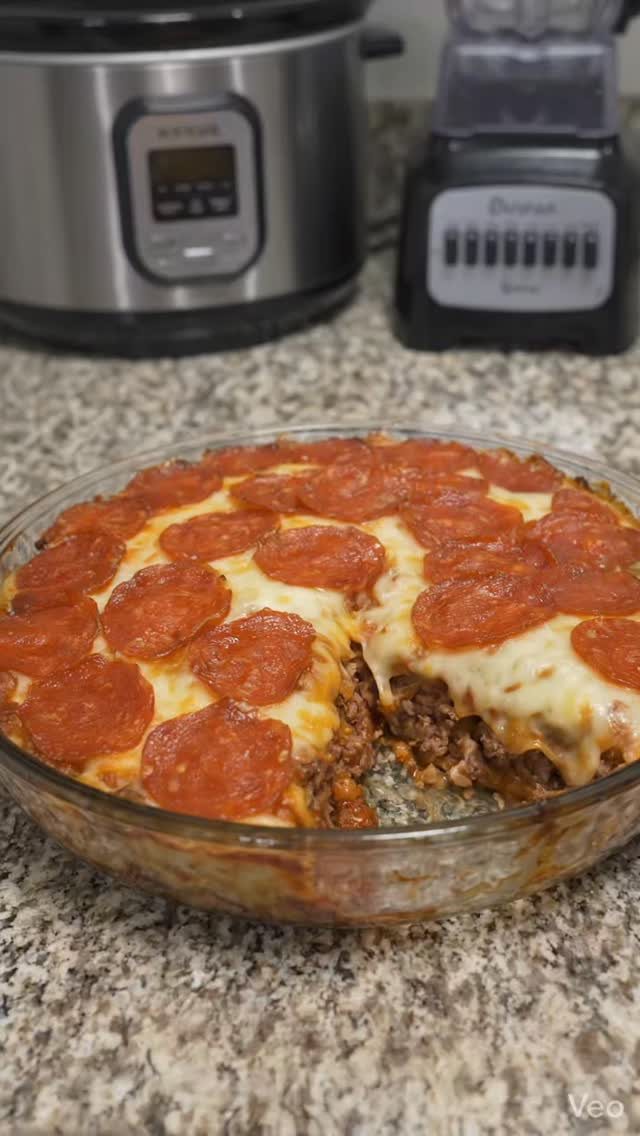 14 Ground Beef Recipes Using Few Ingredients for Low-Stress Weeknights 9 Pizza casserole with melted cheese and pepperoni in a glass dish on a granite countertop.