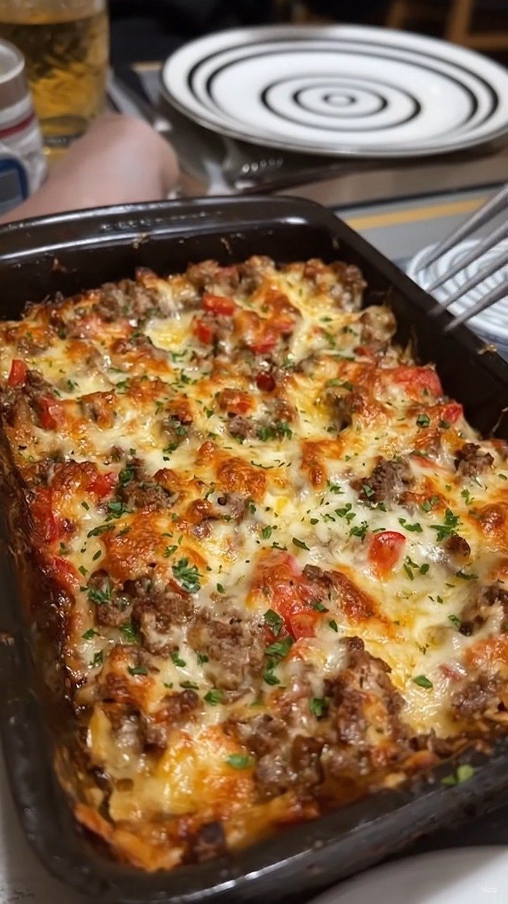 14 Ground Beef Recipes Using Few Ingredients for Low-Stress Weeknights 6 A baked casserole with ground beef, melted cheese, and red peppers in a black dish.