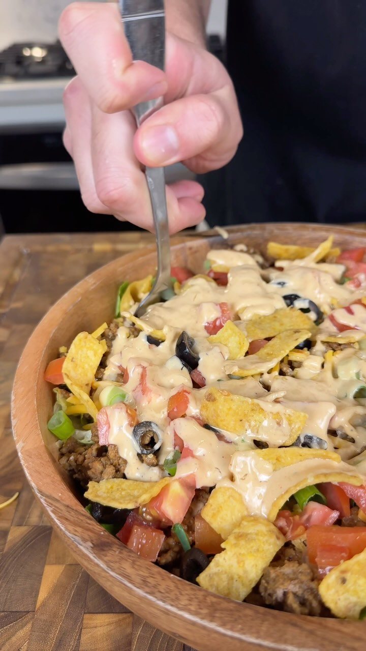 14 Ground Beef Recipes Using Few Ingredients for Low-Stress Weeknights 8 A person eating taco salad with ground beef, chips, and tomatoes from a wooden bowl.